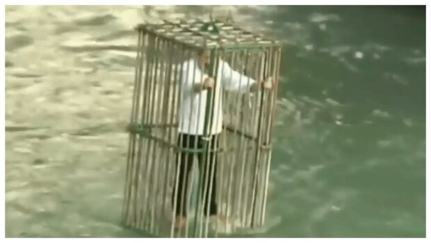 Politiker in einem Käfig in den Fluss hinabgelassen. Quelle: Screenshot YouTube